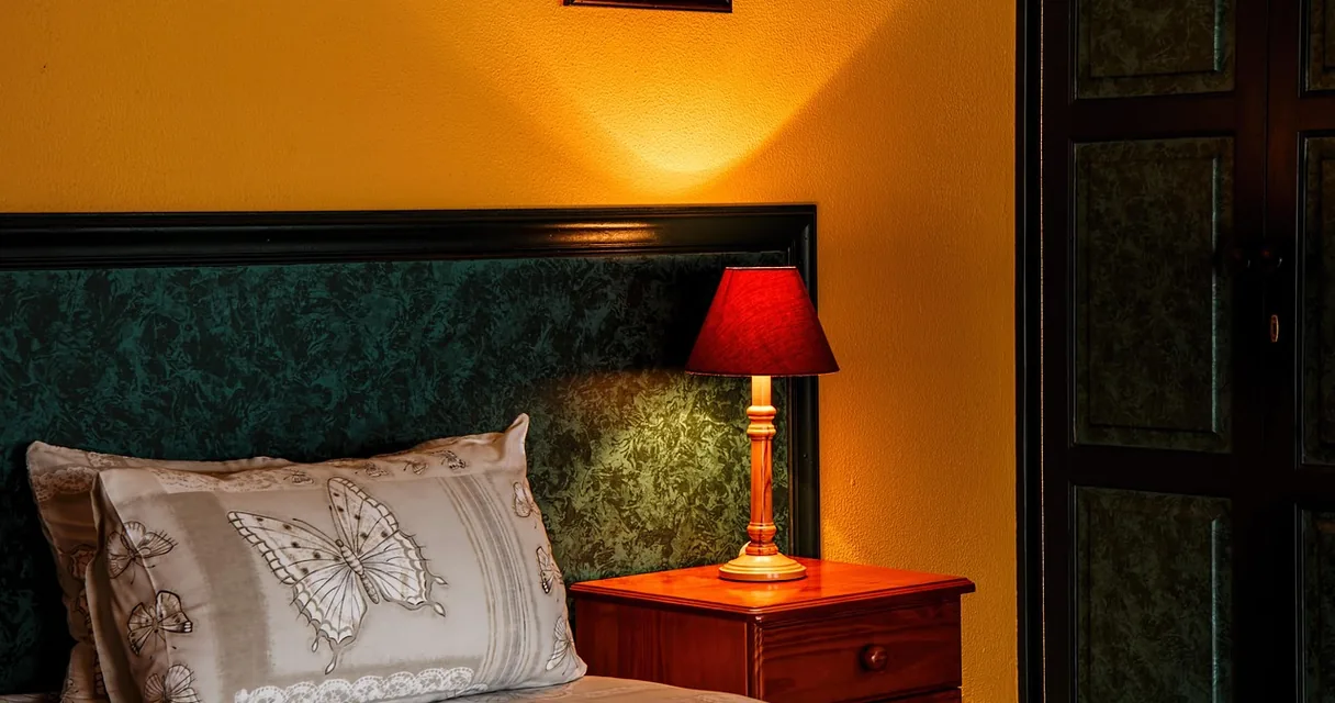Quarto com cama, abajur aceso e travesseiro bordado, ilustrando a azia à noite