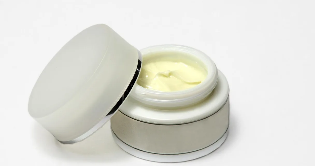 Pote de creme branco aberto sobre fundo claro, ilustrando o tratamento para firmar a pele do rosto